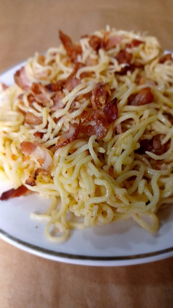Bacon noodles in a white plate on a brown background.