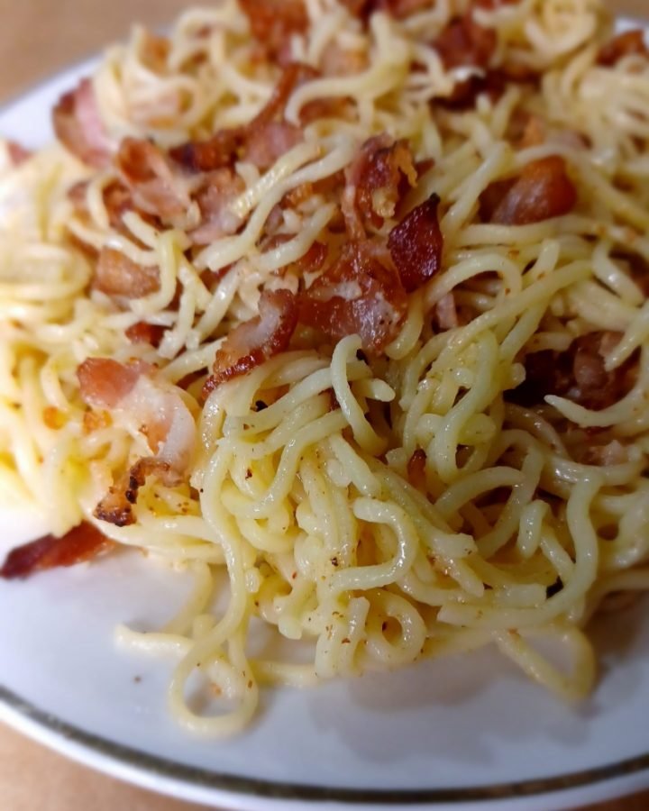 Bacon noodles in a white plate on a brown background.
