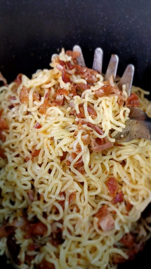 Bacon noodles in a pot with a pasta serving fork.