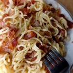 Bacon noodles on a white plate and a fork on a brown background.
