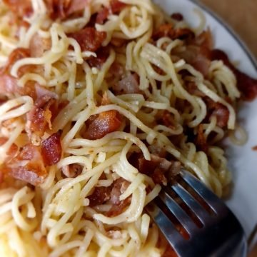 Bacon noodles on a white plate and a fork on a brown background.
