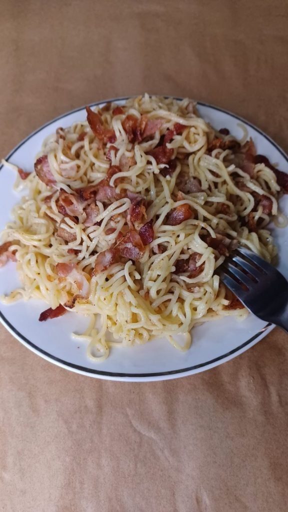 Bacon noodles served in a white dish on a brown background.