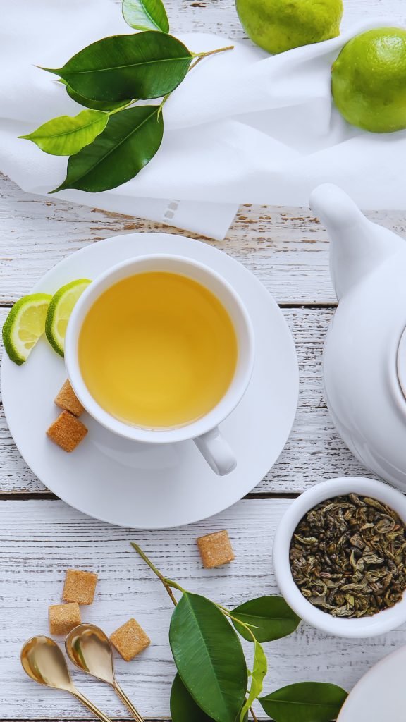 Green tea and limes in a tea cup on a white table.