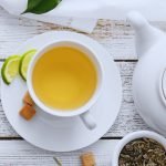 Green tea and limes in a tea cup on a white table.