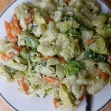 Macaroni salad in a white dish with a fork on a wooden board.