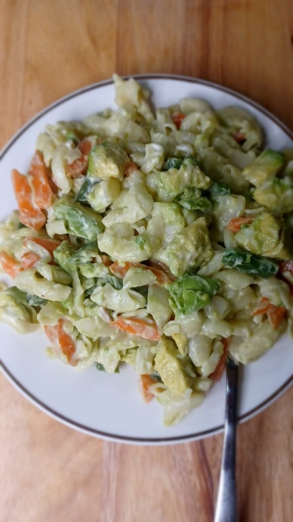 Macaroni salad in a white dish with a fork on a wooden board.