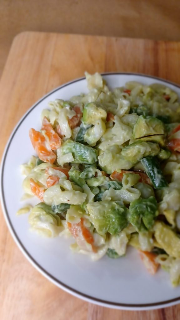Macaroni salad in a white dish on a brown board.