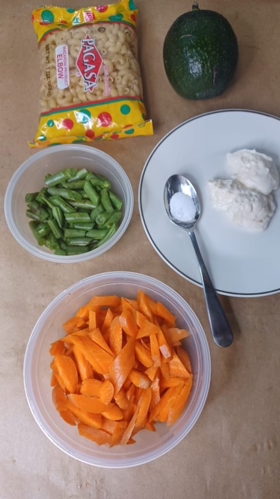 Chopped carrots, green beans, salt, macaroni and mayonnaise on a brown background.