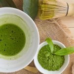 Match tea, matcha power, matcha leaves and wooden brush on a brown background.