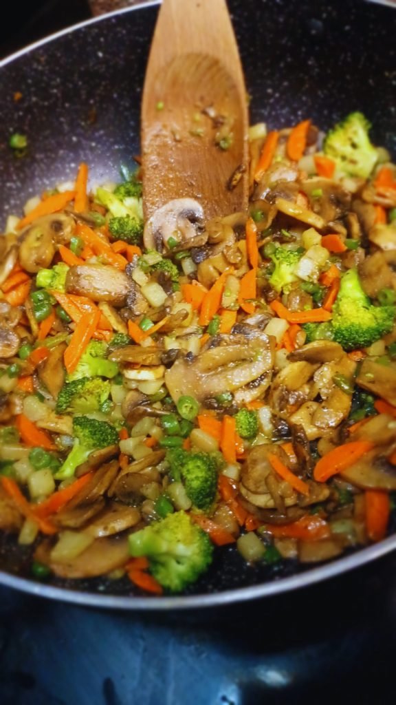 Mushroom stir fry in a pot with a wooden spoon.