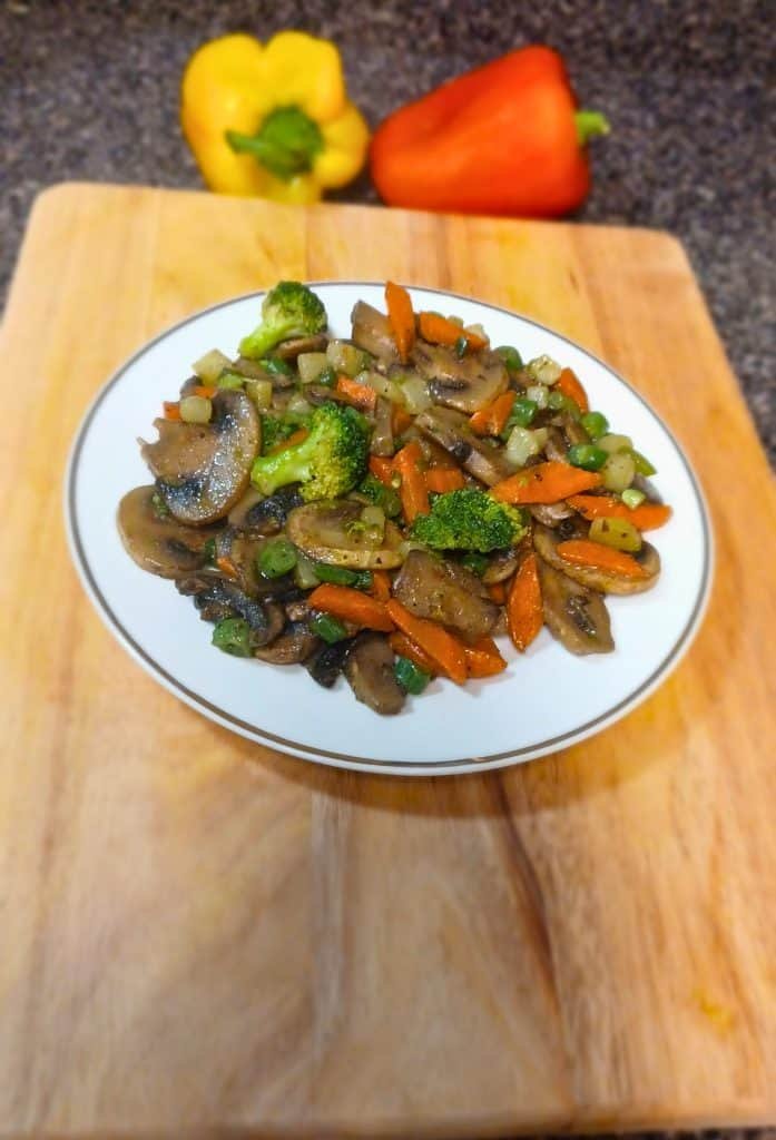 Mushroom stir fry in a white plate on a wooden board with yellow and red chili pepper.