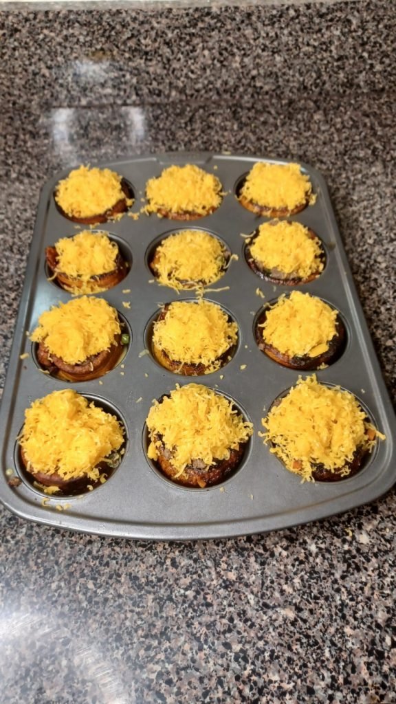 Cheese topped cupcake pan on a gray kitchen slab.