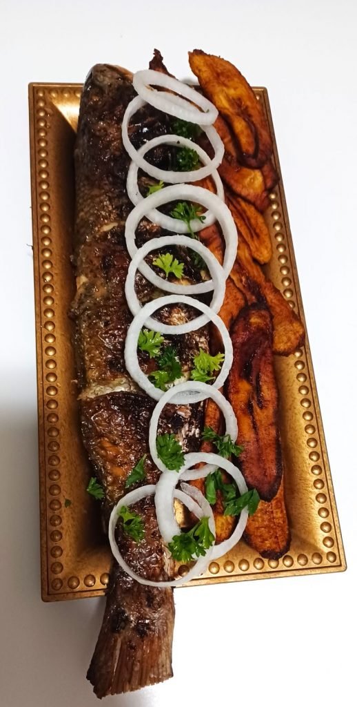 Roasted fish, dodo, onions and some chopped parsley on a brown tray on a white table.