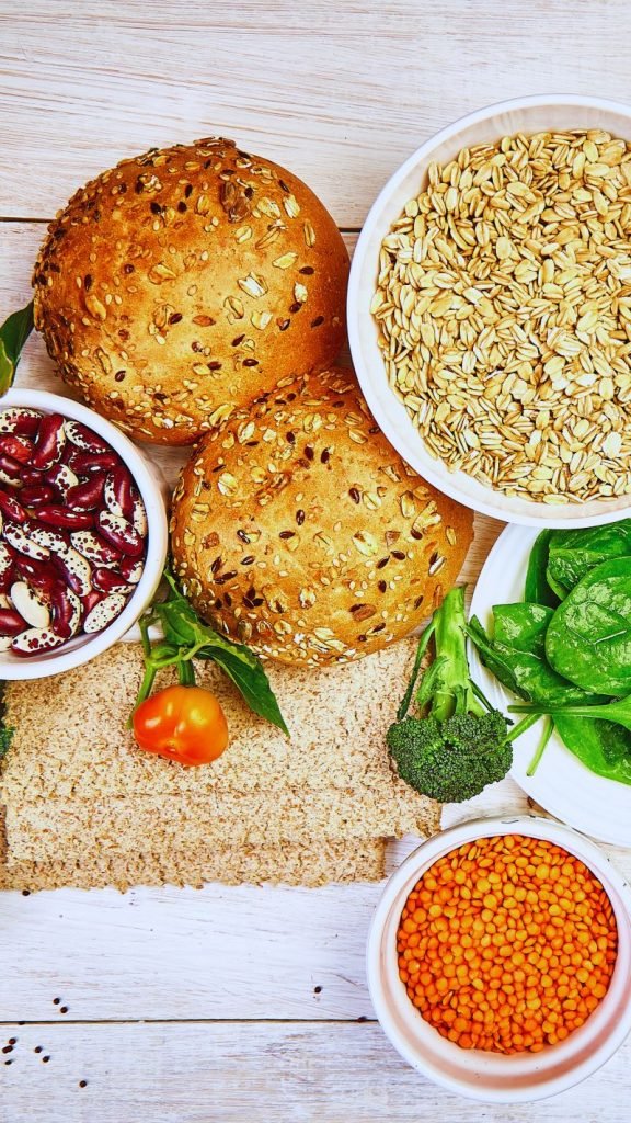 Beans, wheat bread, broccoli, spinach and other fiber rich foods on a white wooden table.