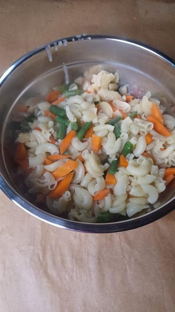 Macaroni, carrots and green beans in a bowl on brown background.