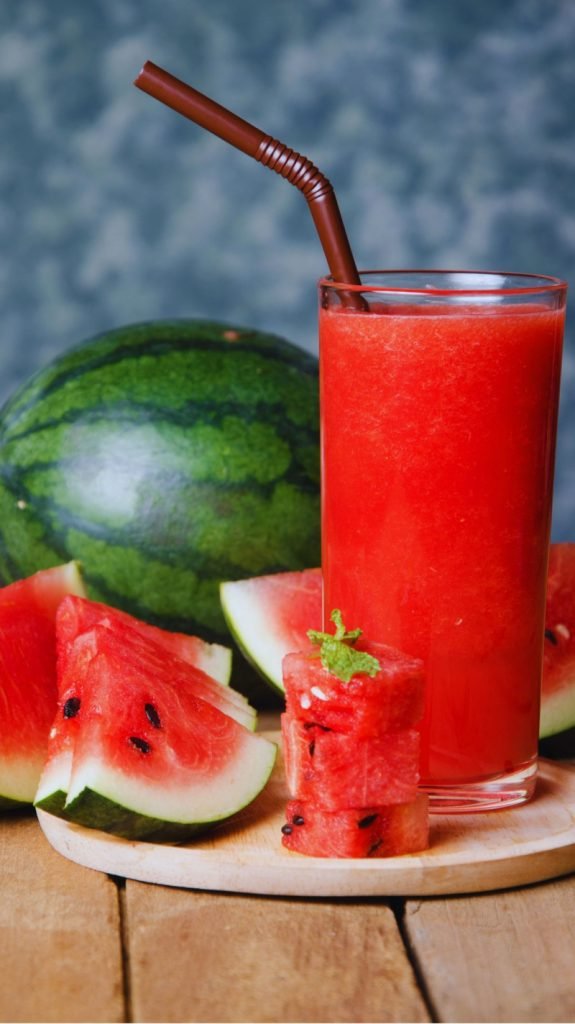 Watermelon juice in a glass with whole watermelon fruit and cut watermelon slices.