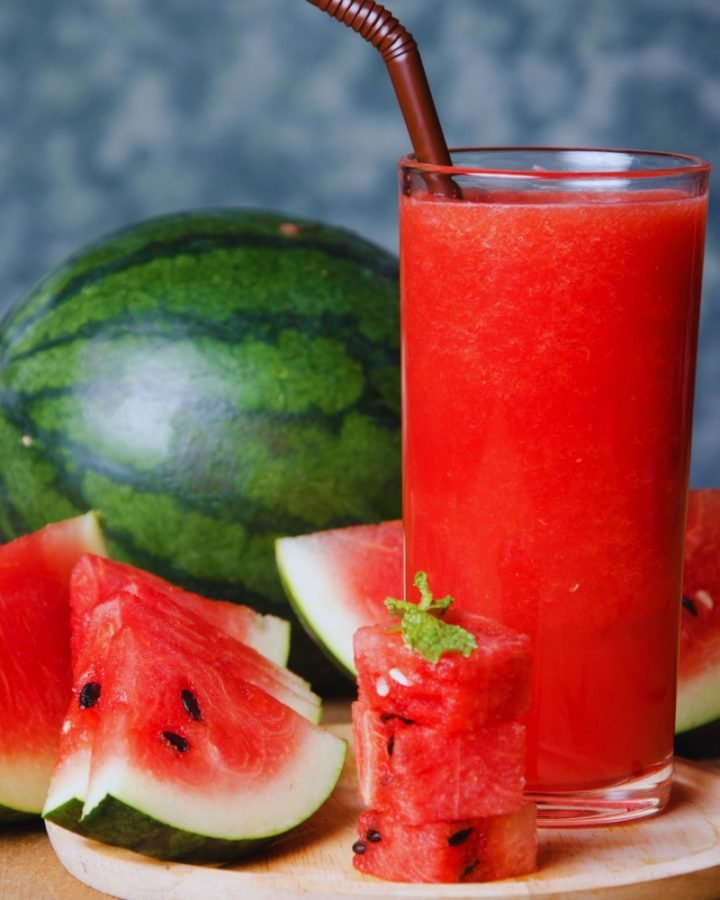 Watermelon juice in a glass with whole watermelon fruit and cut watermelon slices.