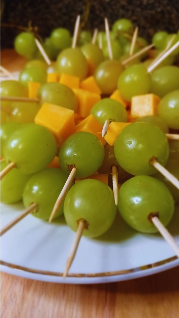 Green grapes and cheese stacked in brochettes in a white dish.
