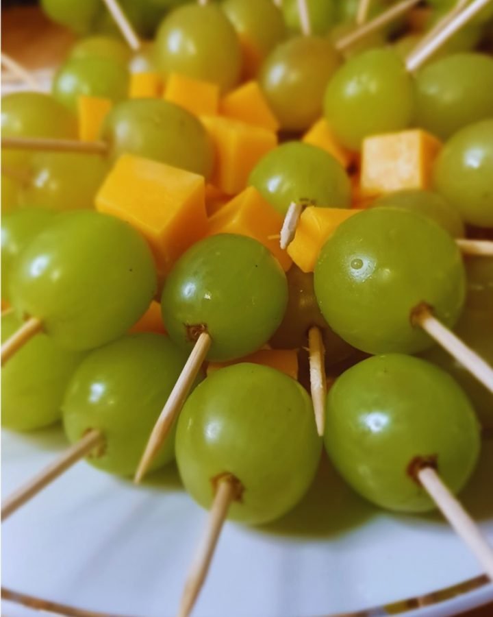 Green grapes and cheese stacked in brochettes in a white dish.