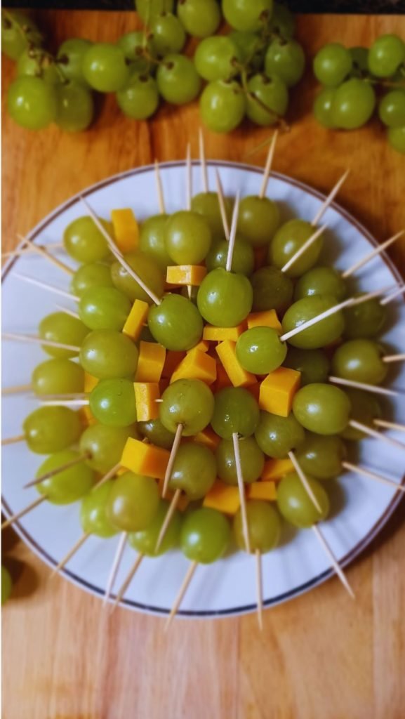 Green grapes and cheese stacked in brochettes in a white plate on a brown board.