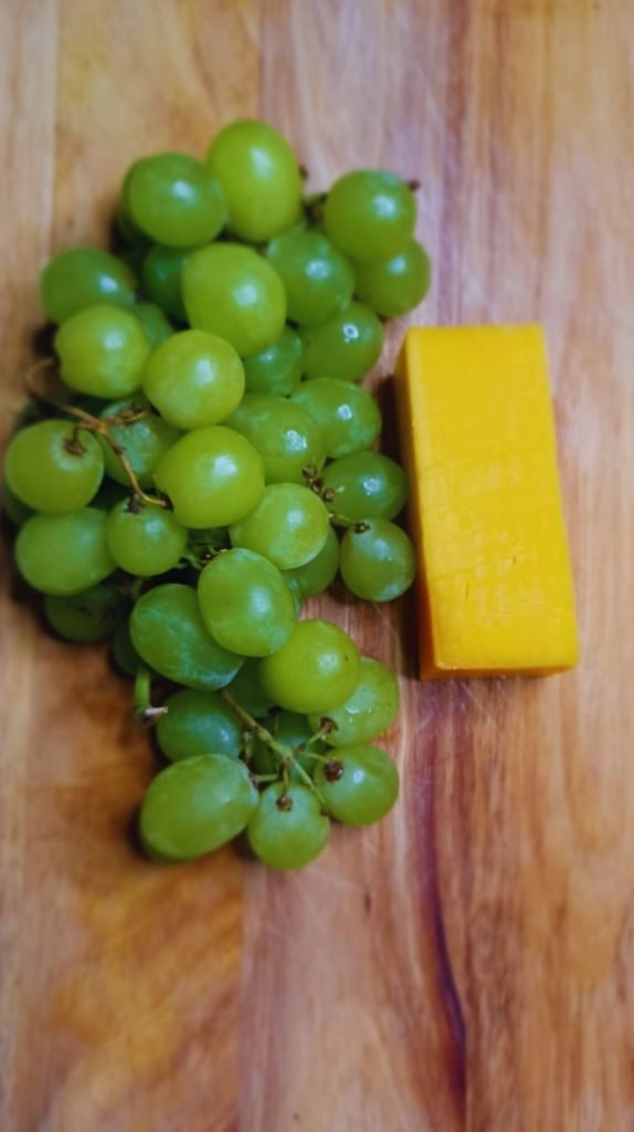 Green grapes and cheese on a brown board.